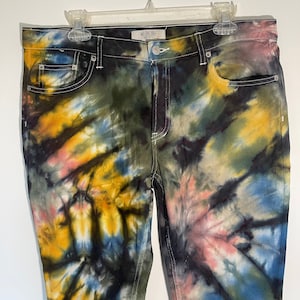 May include: Tie-dye jeans in a variety of colors, including yellow, blue, pink, and green. The jeans have a classic five-pocket design with white stitching and a button closure. The brand name "WE THE FREE" is visible on the waistband.