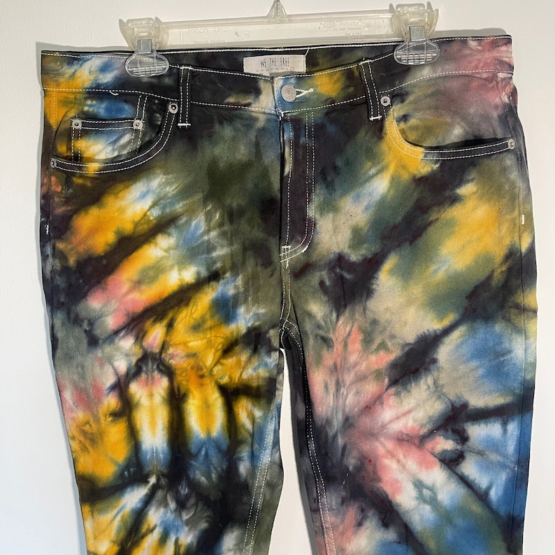 May include: Tie-dye jeans in a variety of colors, including yellow, blue, pink, and green. The jeans have a classic five-pocket design with white stitching and a button closure. The brand name "WE THE FREE" is visible on the waistband.