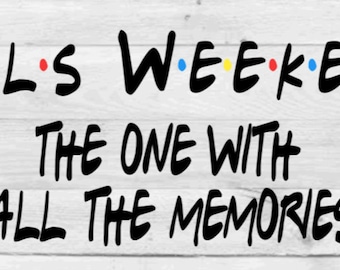 May include: Black and white text graphic on a wood background. The text reads "Girls Weekend The One With All The Memories". The word "Girls" has a red, blue, and yellow dot between each letter. The word "Weekend" has a blue, yellow, and blue dot between each letter.
