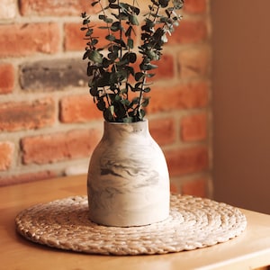 May include: A grey and white marbled ceramic vase with a bouquet of dried eucalyptus branches.