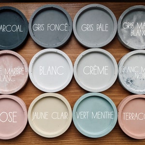 Pu&ograve; includere: Dodici sottobicchieri rotondi in cemento di vari colori e motivi, tra cui carbone, grigio, bianco, crema, rosa, giallo, verde e terracotta. I sottobicchieri sono etichettati con i loro nomi di colore in francese.
