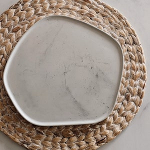 May include: A white ceramic plate with a slightly irregular shape, resting on a woven straw placemat.