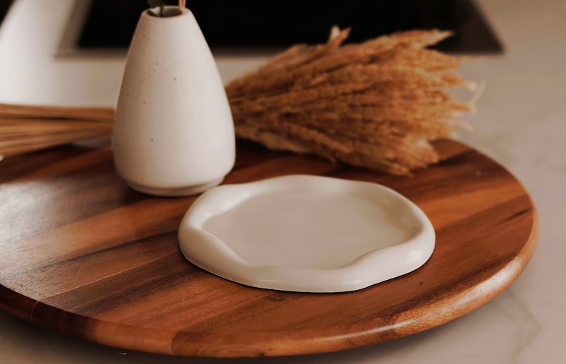 Pu&ograve; includere: Un vaso di ceramica bianca con una piccola pianta all'interno &egrave; posto su un giradischi di legno con un piatto di ceramica bianca. Il giradischi &egrave; circondato da steli di grano secchi.