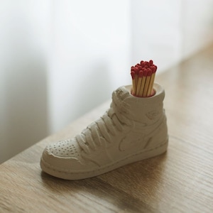 May include: A white ceramic shoe shaped matchstick holder with red tipped matches inside.