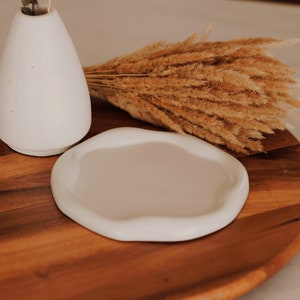 Pu&ograve; includere: Un vaso in ceramica bianca con erba della pampa secca su un vassoio di legno. Il vaso &egrave; rotondo e ha una superficie testurizzata. Il vassoio &egrave; marrone e ha una venatura del legno naturale.