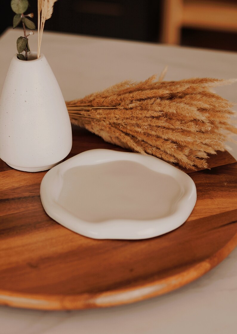Pu&ograve; includere: Un vaso in ceramica bianca con erba della pampa secca su un vassoio di legno. Il vaso &egrave; rotondo e ha una superficie testurizzata. Il vassoio &egrave; marrone e ha una venatura del legno naturale.
