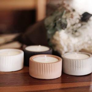 May include: Four concrete candle holders with white, grey, black, and pink wax candles. The candles are on a wooden surface.