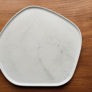 Puede incluir: Un plato de cer&aacute;mica blanco de forma irregular con una superficie ligeramente texturizada. El plato est&aacute; sobre una superficie de madera.