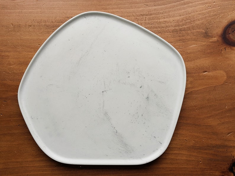 Puede incluir: Un plato de cer&aacute;mica blanco de forma irregular con una superficie ligeramente texturizada. El plato est&aacute; sobre una superficie de madera.
