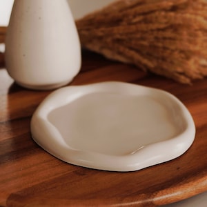 Pu&ograve; includere: Un piatto in ceramica bianca con un bordo ondulato si trova su una superficie di legno. Il piatto &egrave; vuoto e pronto per essere utilizzato.