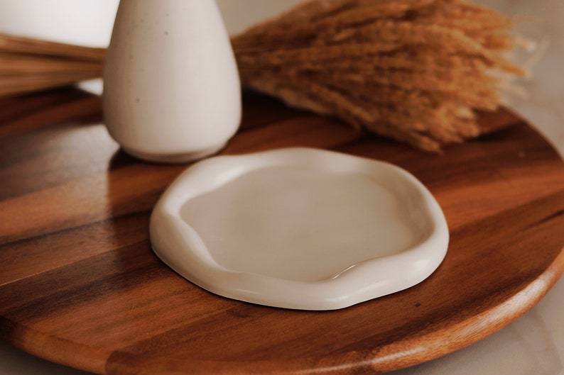 Pu&ograve; includere: Un piatto in ceramica bianca con un bordo ondulato si trova su una superficie di legno. Il piatto &egrave; vuoto e pronto per essere utilizzato.