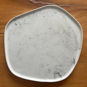 Puede incluir: Un plato de cer&aacute;mica blanco con una forma ligeramente irregular y una superficie texturizada moteada. El plato tiene un aspecto ligeramente desgastado con motas negras en toda la superficie.