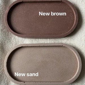Pu&ograve; includere: Due vassoi ovali in cemento. Il vassoio superiore &egrave; marrone e dice "New brown". Il vassoio inferiore &egrave; di un marrone pi&ugrave; chiaro e dice "New sand".