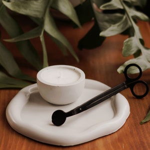 Pu&ograve; includere: Portacandele in ceramica bianca con una candela bianca all'interno. Uno spegnicandele nero &egrave; su un vassoio in ceramica bianca.
