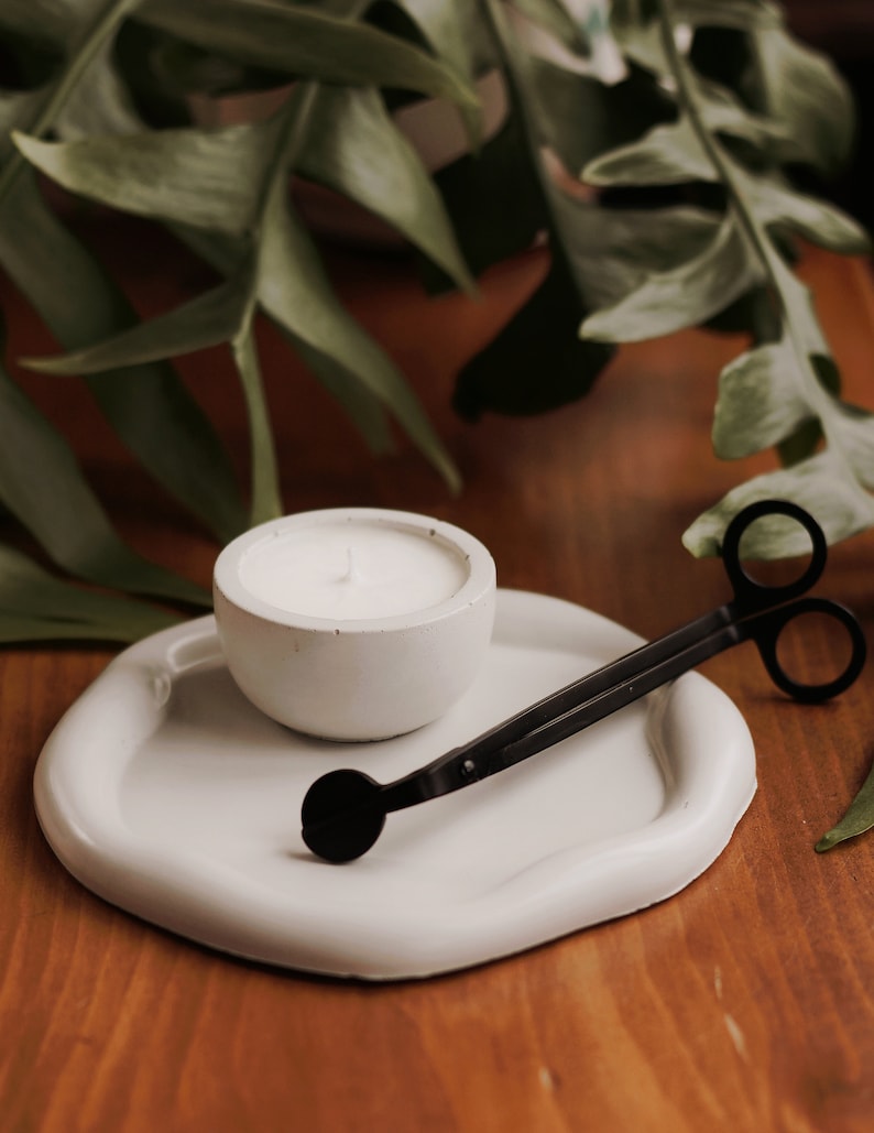 Pu&ograve; includere: Portacandele in ceramica bianca con una candela bianca all'interno. Uno spegnicandele nero &egrave; su un vassoio in ceramica bianca.