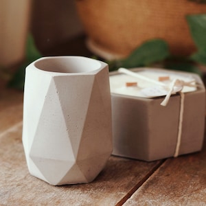 Peut inclure: Deux bougeoirs en béton gris. L'un est de forme géométrique et l'autre est un hexagone. Les deux ont une texture rugueuse.