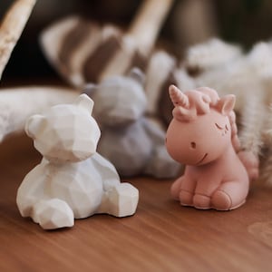 May include: A set of three small, decorative figurines. A white bear, a gray raccoon, and a pink unicorn. The figurines are made of a textured, ceramic-like material.