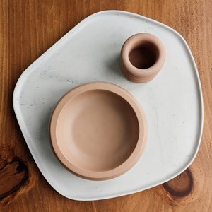 Puede incluir: Una bandeja de cer&aacute;mica blanca con un acabado moteado, que presenta un cuenco de cer&aacute;mica marr&oacute;n claro y un cilindro de cer&aacute;mica marr&oacute;n claro m&aacute;s peque&ntilde;o.