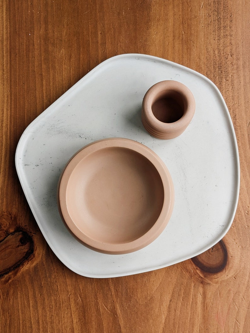 Puede incluir: Una bandeja de cer&aacute;mica blanca con un acabado moteado, que presenta un cuenco de cer&aacute;mica marr&oacute;n claro y un cilindro de cer&aacute;mica marr&oacute;n claro m&aacute;s peque&ntilde;o.