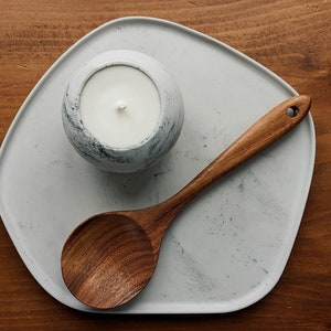 Puede incluir: Una bandeja de cer&aacute;mica blanca con una cuchara de madera y una vela blanca con un acabado moteado gris.