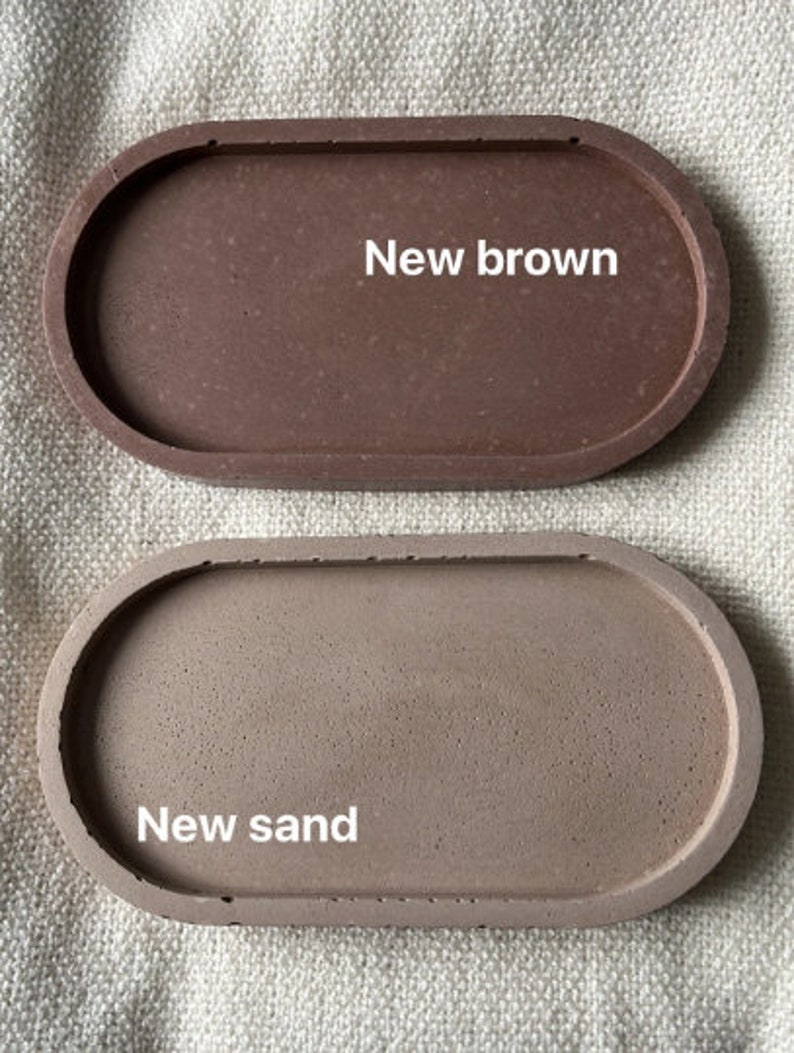 Może przedstawiać: Dwa owalne betonowe tace. G&oacute;rna taca jest brązowa z nadrukiem "New brown". Dolna taca jest jaśniejsza, z nadrukiem "New sand".