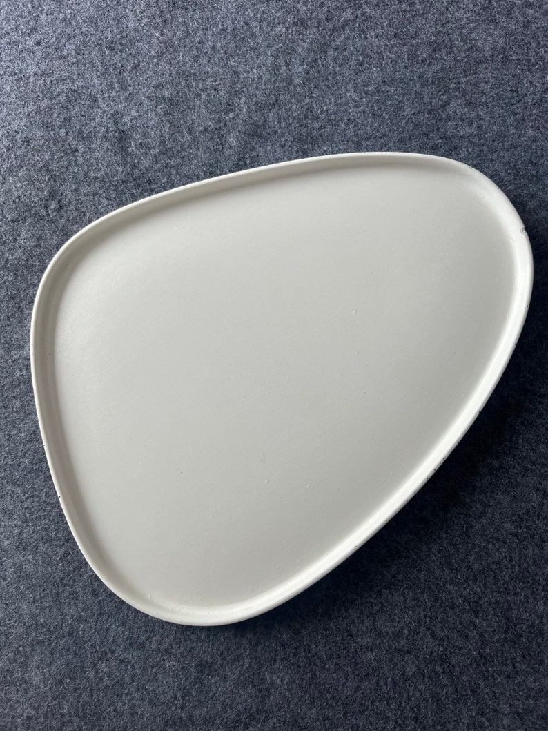 Może przedstawiać: Biała ceramiczna taca do serwowania o nieregularnym, organicznym kształcie. Taca jest gładka i ma lekko fakturowaną powierzchnię.