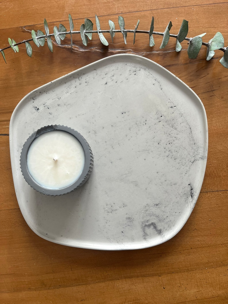 Puede incluir: Una bandeja de cer&aacute;mica blanca con un dise&ntilde;o gris moteado. Un peque&ntilde;o portavelas gris con una vela blanca est&aacute; en la bandeja.