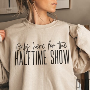 May include: A beige sweatshirt with the text "Only here for the HALFTIME SHOW" printed in black.