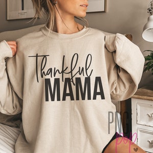May include: A beige sweatshirt with the text "thankful MAMA" in black lettering.