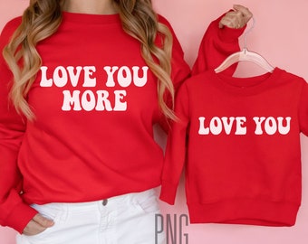 Peut inclure: Deux sweats à manches longues rouges avec du texte blanc. Le plus grand sweat dit "Love You More" et le plus petit sweat dit "Love You".