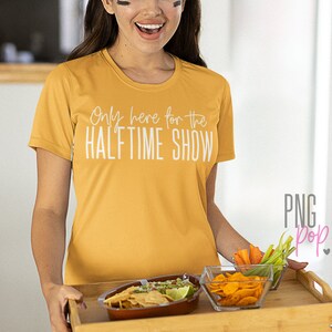 K&ouml;nnte beinhalten: Eine Frau tr&auml;gt ein gelbes T-Shirt mit dem Text "Only here for the HALFTIME SHOW" und h&auml;lt ein Holztablett mit einer Sch&uuml;ssel Guacamole und Chips, einer Sch&uuml;ssel Chips und einer kleinen Sch&uuml;ssel Gem&uuml;se.