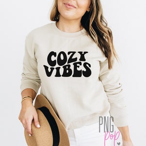 Puede incluir: Una sudadera beige con texto negro que dice "Cozy Vibes" en una fuente retro.