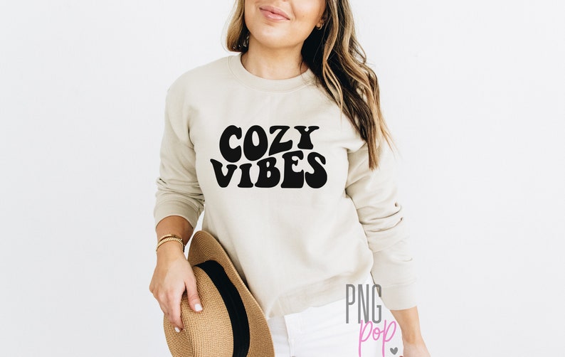 Puede incluir: Una sudadera beige con texto negro que dice "Cozy Vibes" en una fuente retro.