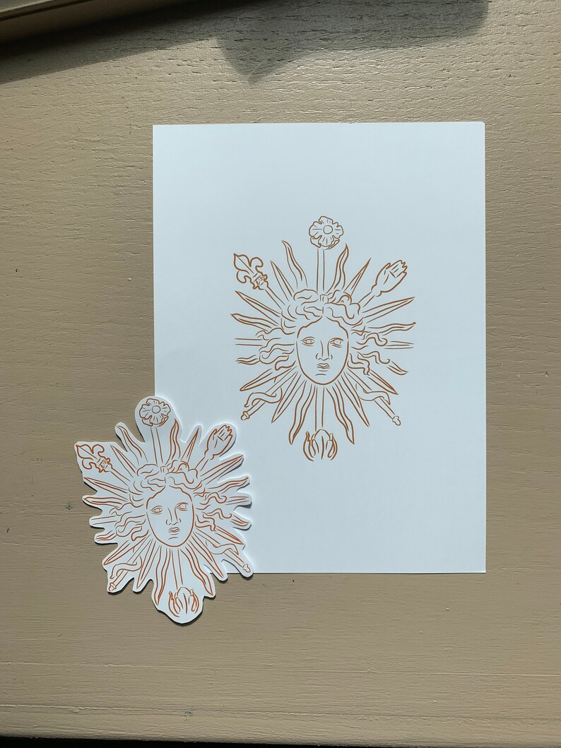 K&ouml;nnte beinhalten: Ein Aufkleber und ein Druck einer Sonne mit einem Gesicht, umgeben von Strahlen und stilisierten Blumen. Das Design ist in brauner Farbe auf wei&szlig;em Hintergrund.