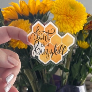 May include: A clear sticker with a honeycomb pattern and the text "Don't be a buzzkill" in black script. The sticker is on a yellow background and has a watercolor effect.
