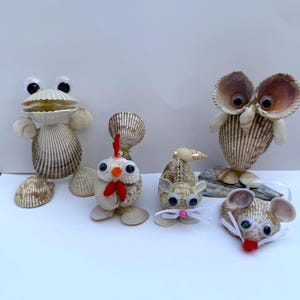 May include: A collection of seashell animal figurines, including a frog, chicken, mouse, and owl. The frog has large googly eyes and a wide mouth. The chicken has a red wattle and comb. The mouse has a pink nose and whiskers. The owl has large, round eyes.
