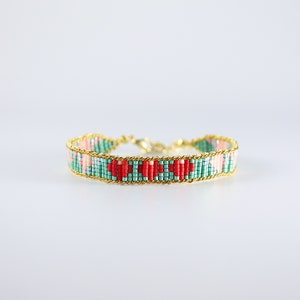 May include: A beaded bracelet with a geometric pattern of red, pink, and green beads. The bracelet is accented with a gold chain.