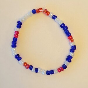 Pu&ograve; includere: Un braccialetto di perline bianche, blu e rosse. Le perline sono disposte in un motivo ripetitivo.