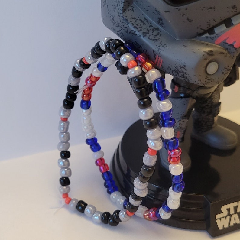 Pu&ograve; includere: Tre braccialetti di perline in nero, bianco, blu, rosso e arancione. I braccialetti sono sovrapposti.