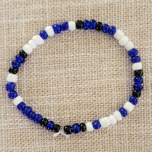 Pu&ograve; includere: Un braccialetto di perline blu, bianche e nere. Il braccialetto &egrave; fatto di piccole perline rotonde che sono infilate insieme in un motivo ripetitivo.