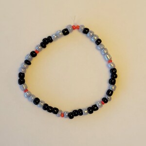 Pu&ograve; includere: Un braccialetto con perline nere, argentate e arancioni.