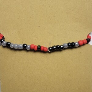 Puede incluir: Primer plano de una pulsera de cuentas con cuentas rojas, grises y negras alternas.