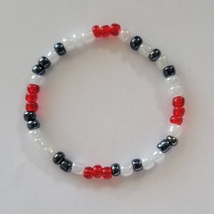 May include: A white, red and black beaded bracelet. The bracelet is made with small round beads and has a simple design.