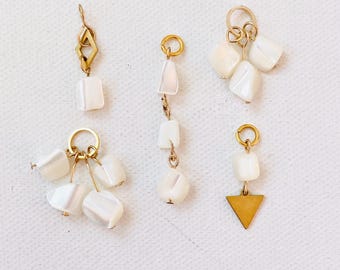 May include: A collection of five unique earrings. Each earring features a gold-colored metal design with white, irregularly shaped beads. One earring has a gold triangle pendant. The earrings are displayed on a white surface.