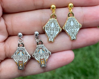 May include: A pair of earrings featuring a white and gold spaceship design. The earrings are silver and gold in color.