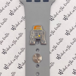 May include: A gray silicone Apple Watch band with a silver metal band connector and a silver metal pin with a yellow and orange robot design.