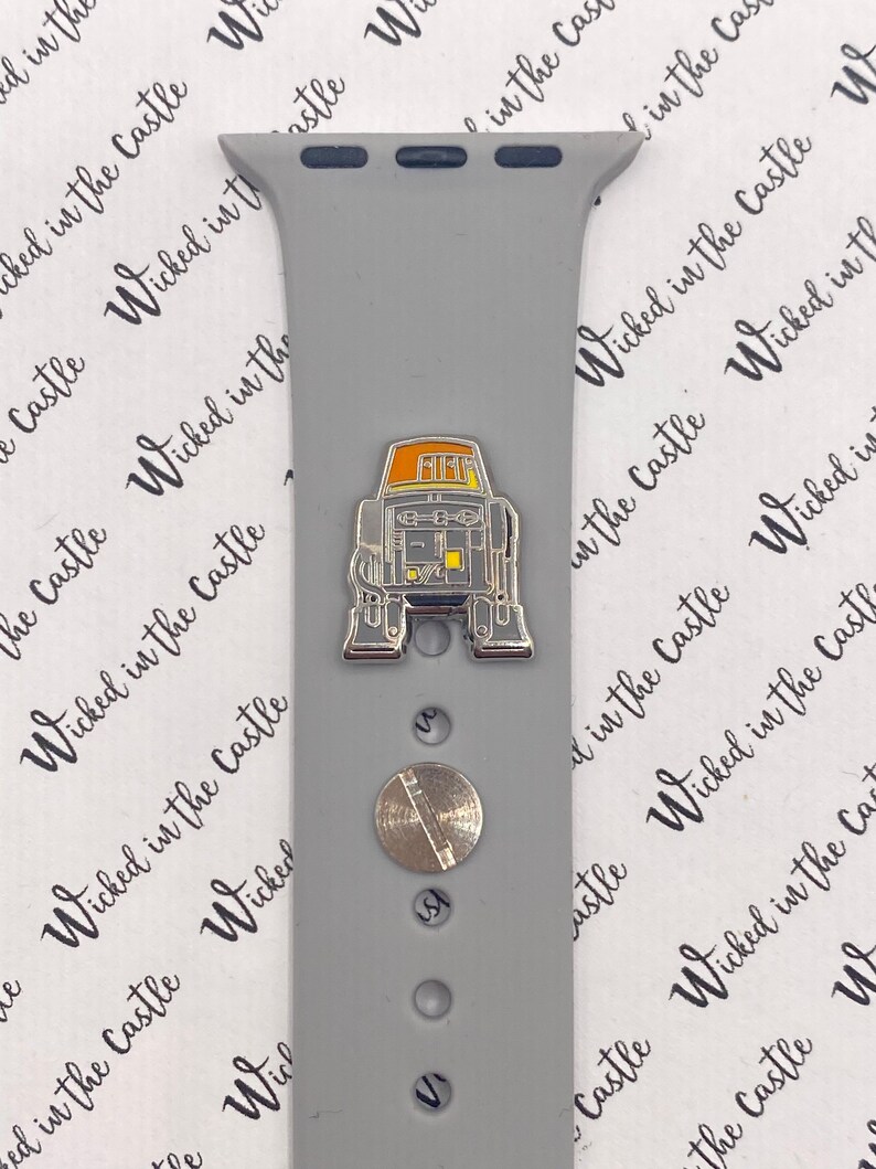 May include: A gray silicone Apple Watch band with a silver metal band connector and a silver metal pin with a yellow and orange robot design.