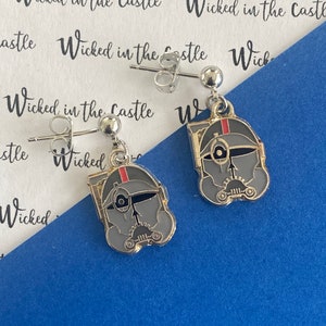 May include: A pair of silver stud earrings with a grey and red cartoon character pendant. The character has a helmet with a visor and a black eye.