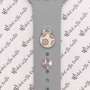 May include: A gray Apple Watch band with a silver and white BB-8 character charm. The band has a smooth, matte finish.