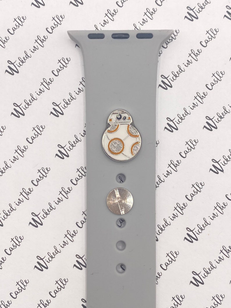 May include: A gray Apple Watch band with a silver and white BB-8 character charm. The band has a smooth, matte finish.